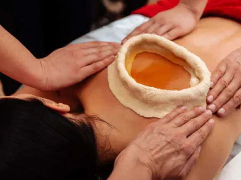 Person receiving a massage with a heart-shaped object on the back filled with ghee 