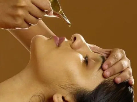 Person receiving a traditional Ayurvedic treatment with oil being applied to the face.