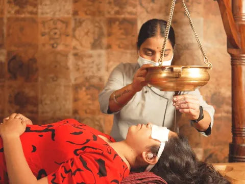 Person receiving a traditional head massage with a bronze bowl in a setting with wooden walls.